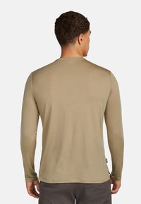 Camicia a maniche lunghe color khaki, con collo rotondo, texture morbida e un design leggermente aderente, con un'etichetta visibile sul lato sinistro in basso.