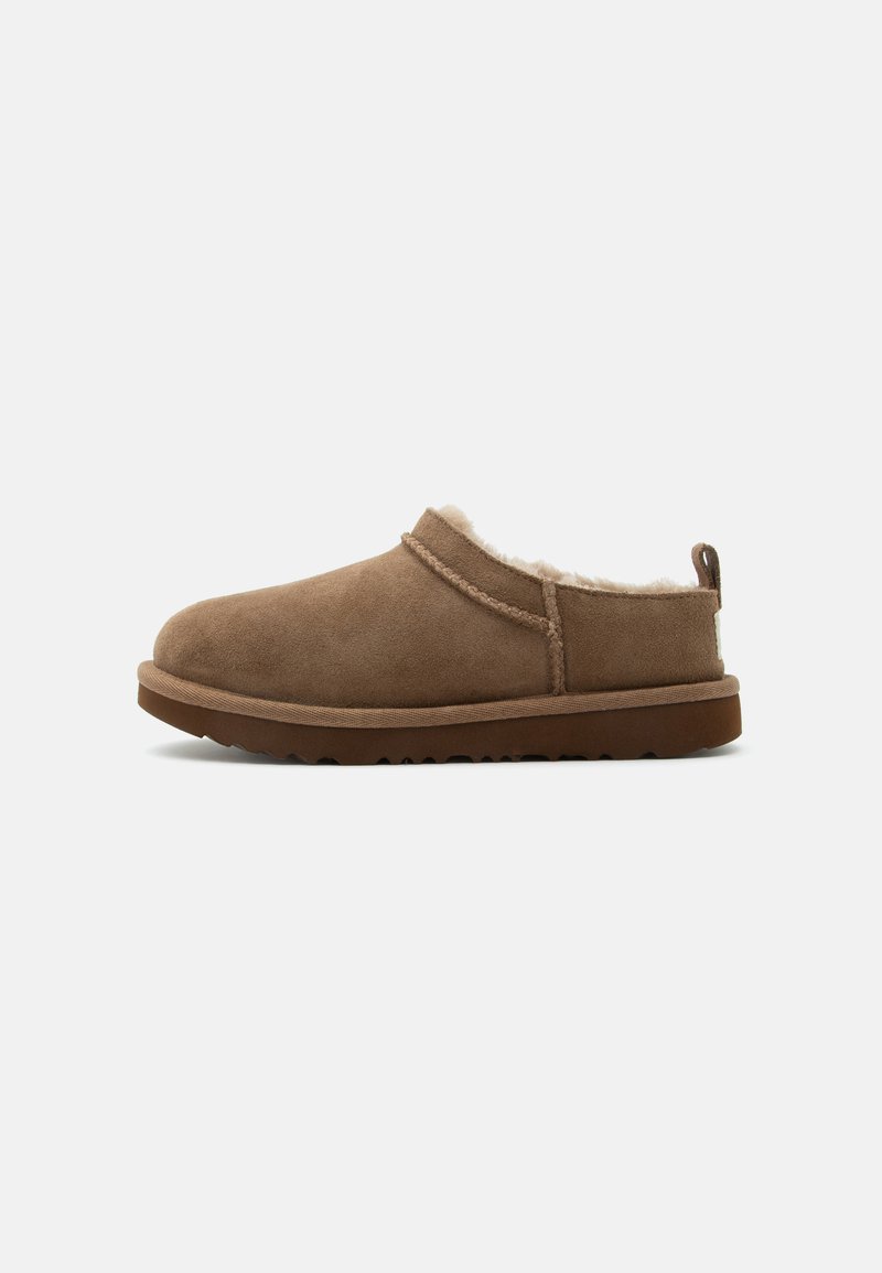 Chausson marron en daim à enfiler avec doublure crème en peluche et semelle en caoutchouc marron, présenté de côté sur un fond clair.