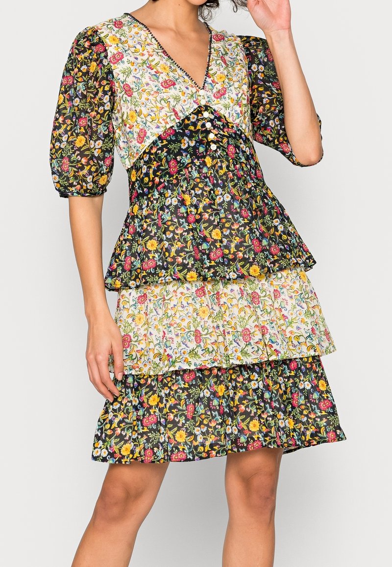Blumenkleid mit V-Ausschnitt, ausgestattet mit schwarzen, weißen und blumigen Lagen, Puffärmeln und einer taillierten Taille. Zarte Druckmuster mit lebhaften Farben.