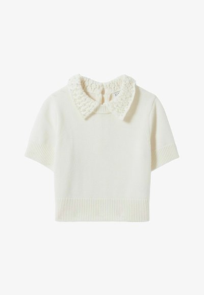 Suéter corto de manga corta en color crema. Presenta un cuello texturizado de punto con acentos de cuentas. Dobladillo ribeteado y puños de las mangas ribeteados.