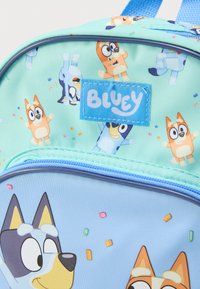 Ανοιχτό μπλε σακίδιο με πολύχρωμους καρτούν χαρακτήρες, σε φόντο μέντας πράσινου χρώματος και παιγνιώδες μοτίβο με κομφετί. Μπλε φερμουάρ κλεισίματος.