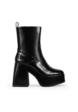 Bottine plateforme noir brillante avec un talon épais, texture lisse, couture sur le côté et une languette à l'arrière pour un enfilage facile.