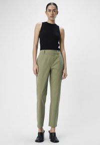 Un haut sans manches noir à côtes associé à un pantalon tailleur vert clair. Le pantalon présente une jambe fuselée et des poches latérales. Des mules noires à talons sont portées.