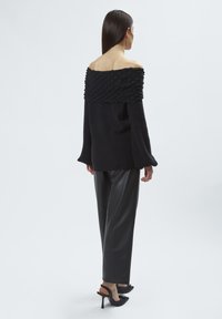 Schwarzer Carmenpullover mit strukturiertem Rippenhalsausschnitt, langen Ärmeln, kombiniert mit hochgeschnittenen schwarzen Kunstlederhosen und Absätzen.