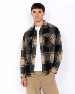 Sort og gul ternet flannel skjorte med to brystlommer og sorte knapper, parret med en hvid t-shirt og lyse khaki bukser.