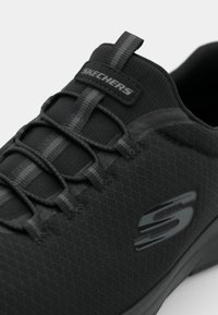 Black athletic shoe featuring a textured upper, elastic laces, and a branded logo on the side. The design is minimalistic and streamlined.