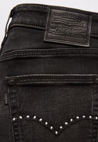 Jeans de mezclilla negra con un parche de cuero de la marca, costuras en contraste y acentos de remaches plateados en los bolsillos traseros.