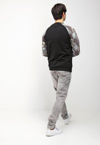 Sudadera negra con mangas de color gris con patrón, combinada con pantalones gris claro y zapatillas blancas, vista desde la parte de atrás. Texturas suaves y corte informal.