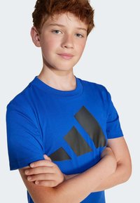 Mėlynas medvilninis marškinėliai trumpomis rankovėmis, su dideliu juodu trikampiu logotipu priekyje. Minkšta tekstūra ir reguliaraus fasono dizainas.