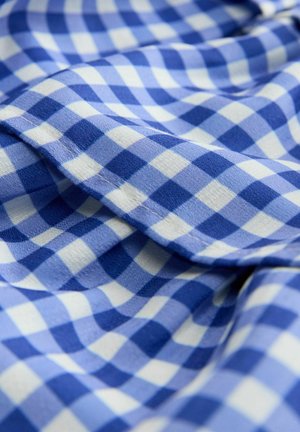 Modro-bílá kostkovaná tkanina s měkkou strukturou, zdobená vlnitým okrajem a překrývajícími se vrstvami. Vzor se střídá mezi světlými a tmavými odstíny.