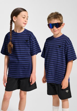 To børn bærer store mørkeblå t-shirts med sorte striber. Pigen har langt hår i en fletning, og drengen bærer reflekterende solbriller. Begge har sorte shorts på.