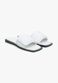 Białe klapki z szerokim, wyściełanym paskiem, gładkim syntetycznym materiałem i płaską czarną podeszwą. Prosty, nowoczesny design o kwadratowym kształcie.