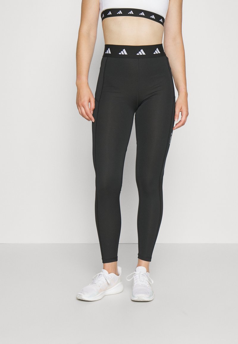 Leggings sportivi neri con un'alta vita caratterizzati da un motivo con logo, realizzati in un tessuto liscio e elasticizzato, abbinati a sneakers bianche.