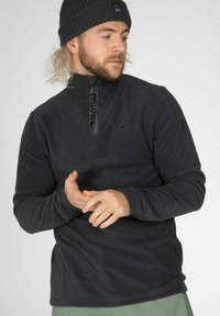 Pullover in pile nero con colletto alto e zip a metà, caratterizzato da un dettaglio del logo sul nastro della zip. Texture morbida e maniche lunghe.