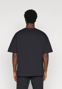 Melns kokvilnas T-krekls ar brīvu piegriezumu, īsām piedurknēm un apaļu kakla izgriezumu, ar gludu tekstūru un minimālu šuvju detaļu.