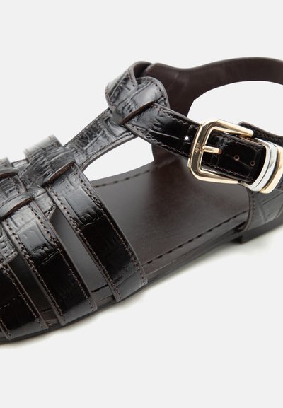 Μαύρο δερμάτινο σανδάλι ψαρά με αγκράφα σε χρυσό τόνο και ραμμένους ανοιχτούς ιμάντες σε επίπεδη σόλα.