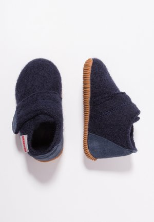 Par navy blå småbørns hjemmesko med velcro stropper og brune gummisåler på hvid baggrund.