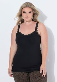 Černý top na ramínka s krajkovými detaily na ramínkách a výstřihu, s uzkým střihem. Nosený s vzorovanými kalhotami.