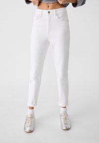 White denim jeans with a high waist, five pockets, and rolled cuffs, paired with silver sneakers and white ankle socks.