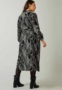 Zwart-wit gestreepte midi-jurk met lange mouwen en een ceintuur in de taille, gekenmerkt door een textuurstof en een vloeiende silhouet, gedragen met zwarte enkellaarsjes.