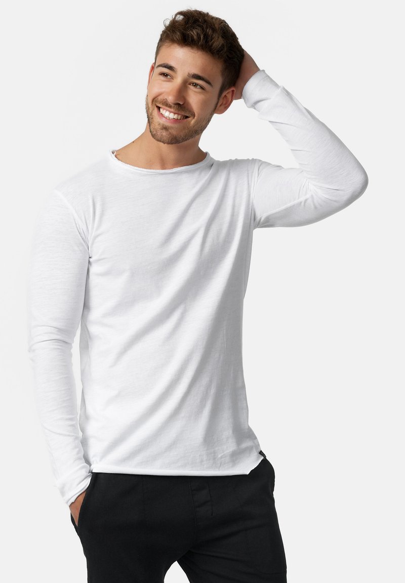 Camiseta blanca de manga larga hecha de tejido ligero, con un escote redondo y un corte relajado, combinada con pantalones negros.