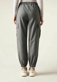Graue Cargo-Hosen mit elastischem Bund, gerippten Bündchen und Seitentaschen, kombiniert mit hellen Sneakers.