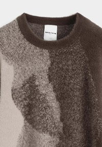 Gros plan sur un pull en maille floue à col rond avec un motif abstrait marron et beige.