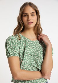 Grüne Blumenbluse mit kurzen puffärmeln, verziert mit Rüschendetails und einem runden Ausschnitt. Hergestellt aus einem leichten, strukturierten Stoff.