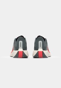 Chaussures de course pour hommes avec une tige en mesh gris, des accents rouges et une semelle rembourrée. Comprend un talon arrondi et une semelle extérieure texturée pour plus de traction.