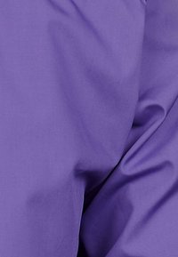 Nahe Aufnahme eines glatten, violetten Stoffs mit sichtbaren Falten und Knicken.