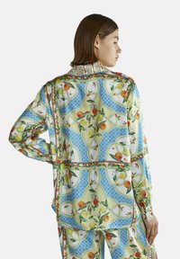 Silke skjorte med levende frugt- og blomstermotiv. Har en blå baggrund, røde detaljer og krave. Lange ærmer, afslappet pasform og glat tekstur.