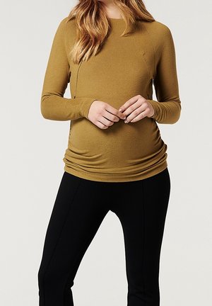 Langärmliges, senfgelb-farbenes Oberteil mit einer figurbetonten Silhouette und gerafftem Seitendetail, kombiniert mit schwarzen Leggings. Weicher, dehnbarer Stoff.
