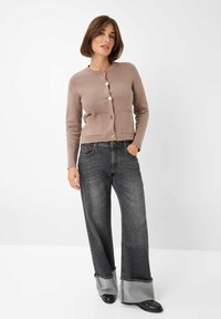 Light brown cardigan with round neckline, front pockets, and gold buttons paired with wide-leg black and gray jeans, featuring a contrasting hem.