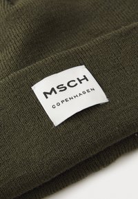 Dark green knit beanie featuring a white fabric label with black text "MSCH COPENHAGEN" and a smooth, textured surface.