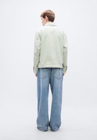 Ανοιχτό πράσινο, χαλαρή εφαρμογή μπουφάν με υπερμεγέθεις ώμους, σε συνδυασμό με τζιν παντελόνια φαρδιάς γραμμής σε μπλε χρώμα με πίσω τσέπες.