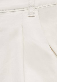 Tessuto beige chiaro con una texture liscia, caratterizzato da pieghe laterali, dettagli di cucitura e una vita con chiusura a un singolo bottone.