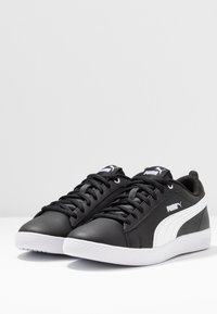 Mustat nahkasneakerit, joissa on valkoinen sivuviiva, litteät nauhat, pyöristetty kärki ja kuvioitu kumipohja. Puma-logo kieliosassa ja sivulla.