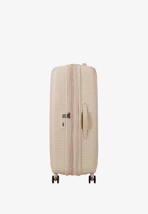 Maleta rígida beige con cuatro ruedas negras, un asa lateral y una cerradura de combinación incorporada.