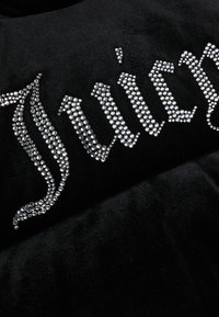 Črn žametni material z bleščečimi rhinestone črkami, ki tvorijo napis "Juicy." Oblikovanje je držno z zapletenimi detajli.