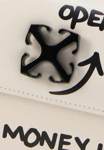 Κοντινή λήψη ενός μαύρου κλεισίματος με τέσσερα αγκίστρια σε λευκό υλικό με μαύρο κείμενο που γράφει «open» και «MONEY» και ένα κυρτό βέλος που δείχνει προς τα πάνω.