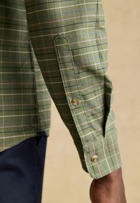 Chemise à carreaux verte avec motifs à carreaux roses clairs, bleus et blancs ; dotée de poignets boutonnés et d'une fente de manche façonnée.