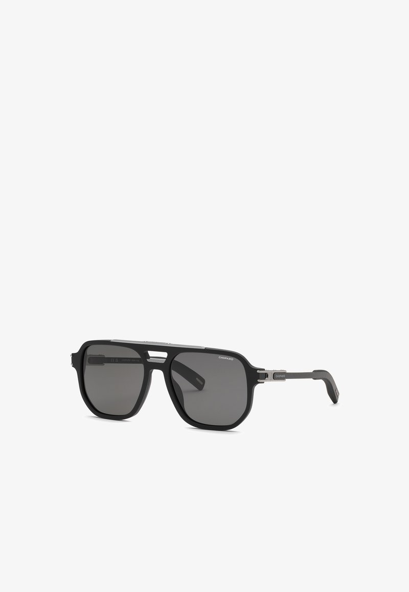 Lunettes de soleil rectangulaires noires avec des verres teintés foncés et des branches fines, avec un petit détail métallique près des charnières et un design à double pont.