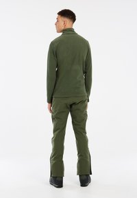 Groene geribbelde lange mouwen top met een hoge kraag, gecombineerd met bijpassende groene cargobroek met ritszakken aan de zijkanten en uitlopende pijpen.
