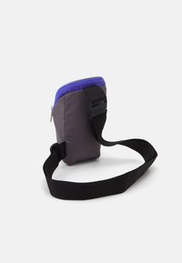 Compact gray bag with a purple zipper, black adjustable strap, and a textured fabric exterior. Features a sturdy buckle on the strap.