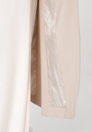 Beiger Stoff mit glänzendem Satinfutter, das ein dezentes Blumenmuster aufweist, dargestellt in einer Nahaufnahme der Kante eines Kleidungsstücks.