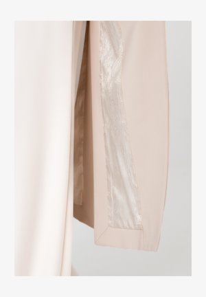 Beiger Stoff mit glänzendem Satinfutter, das ein dezentes Blumenmuster aufweist, dargestellt in einer Nahaufnahme der Kante eines Kleidungsstücks.