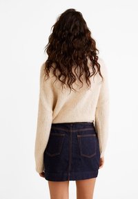 Pull en maille beige à manches larges associé à une mini-jupe en denim foncé. La jupe est dotée de poches arrière et de coutures visibles.