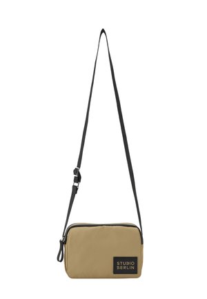 Kleine rechteckige beige Umhängetasche mit schwarzem verstellbarem Riemen und einem schwarzen "Studio Berlin"-Etikett vorne.
