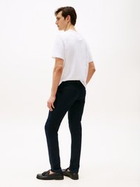 Λευκό βαμβακερό μπλουζάκι, ναυτικά slim-fit παντελόνια και μαύρες loafers. Λείο ύφασμα, απλός σχεδιασμός και ουδέτερη χρωματική παλέτα.