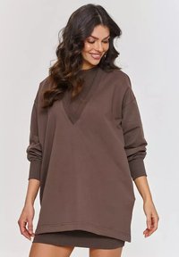 Brązowa, oversize'owa bluza z głębokim dekoltem w serek, długimi rękawami i ściągaczami. Miękka faktura i casualowy design idealny do noszenia w warstwach.